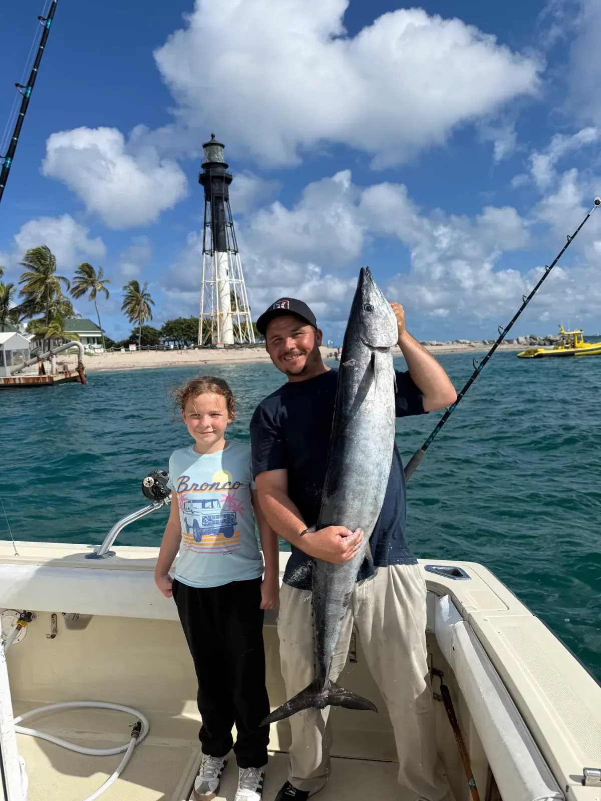 A young angler and the mate holding a wahoo taller than she is, the Hillsboro lighthouse behind them