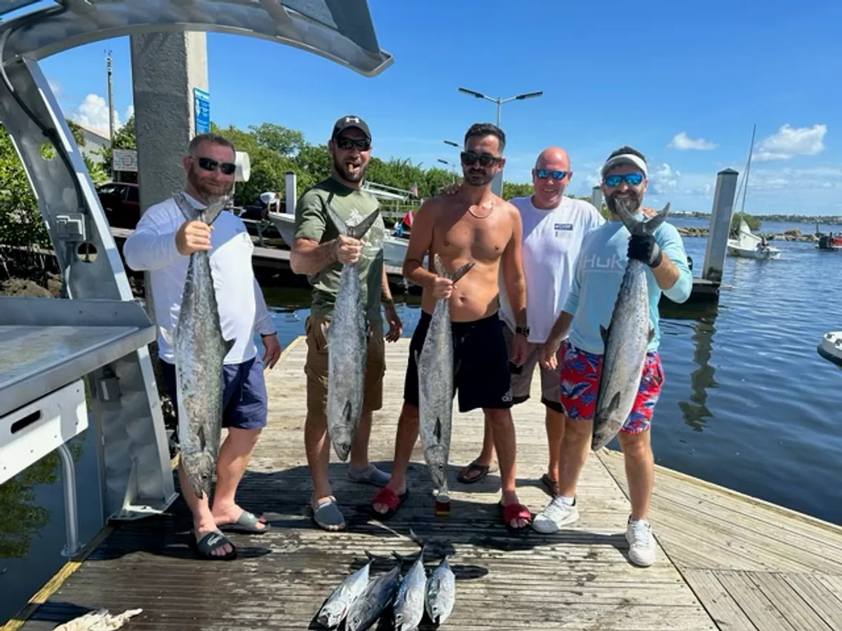 Five anglers on the dock holding up their kingfish after a morning trip