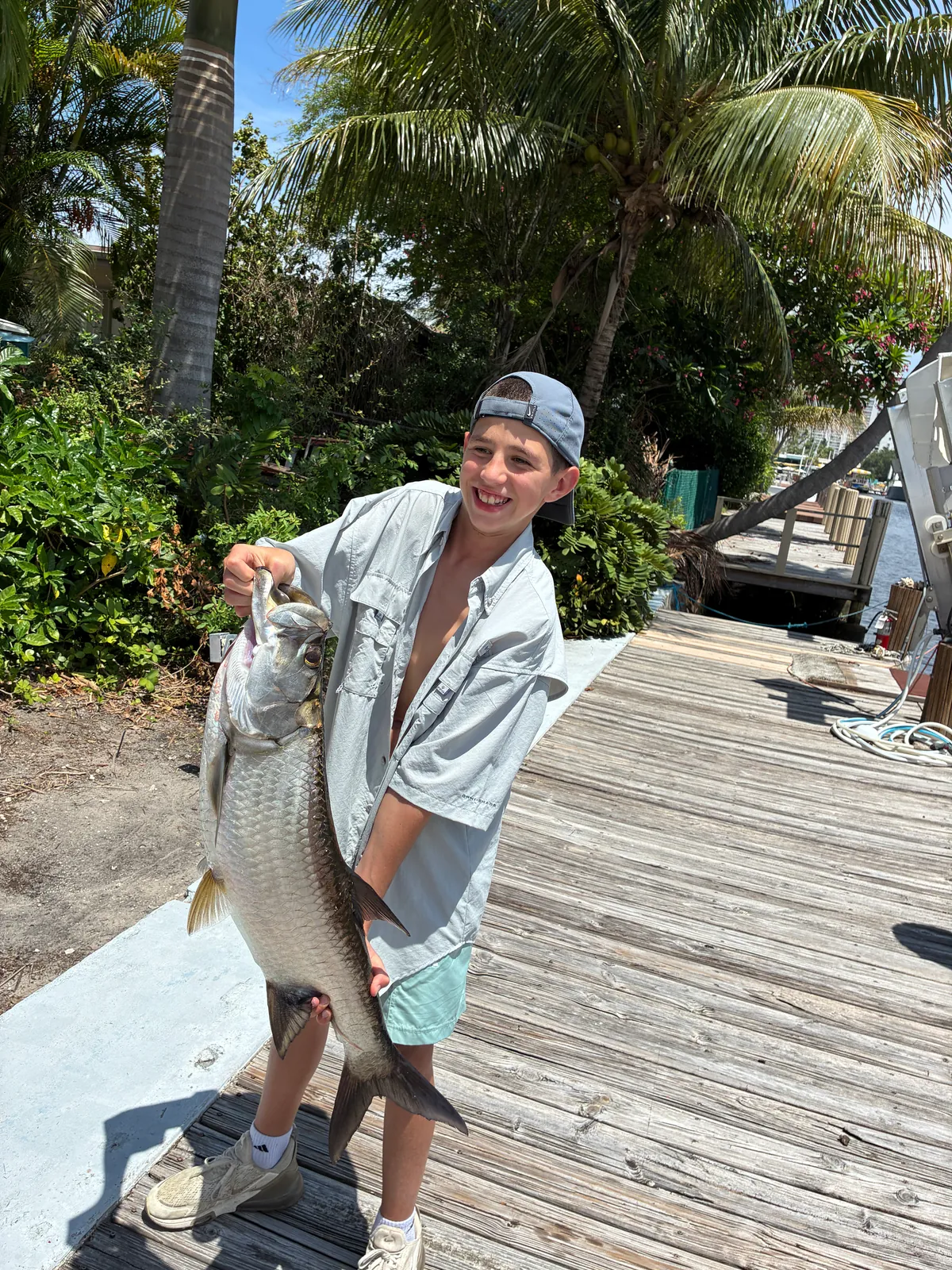 A young angler on the dock holding a tarpon nearly as long as he is tall